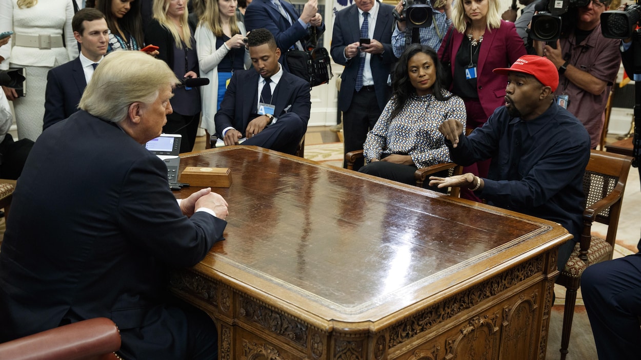 Donald Trump et Kanye West sont assis face à face, entourés de photographes et de journalistes.
