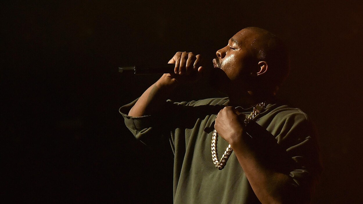 Le rappeur Kanye West chante dans un micro sur scène lors d'un spectacle.