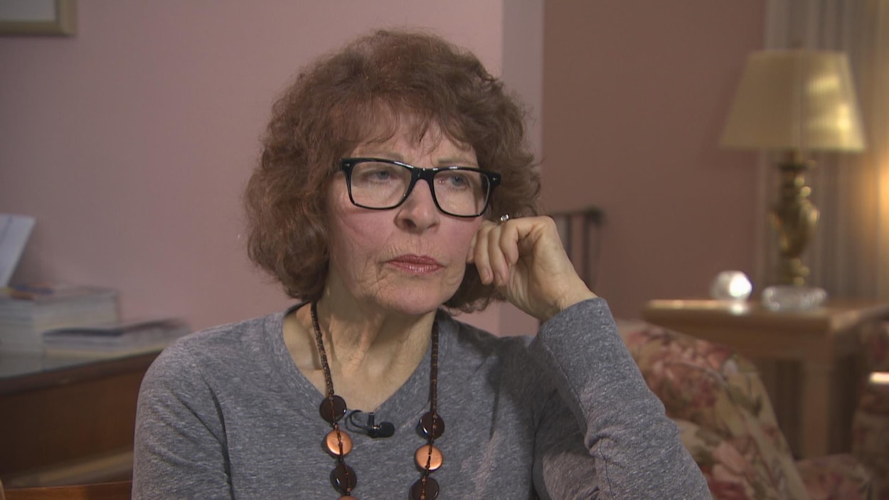 Une femme porte un cardigan gris avec un collier.