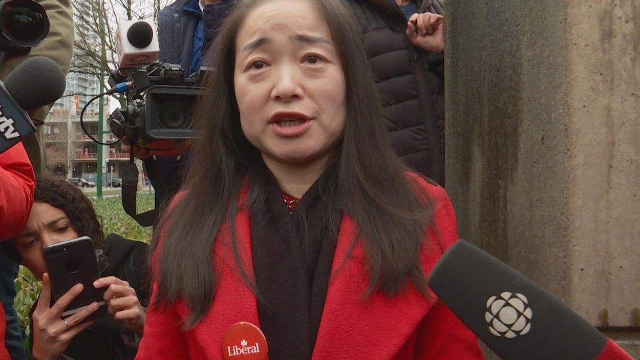Une femme avec un macaron du parti libéral, qui parle devant des micros, des journalistes et des caméras en arrière-plan.