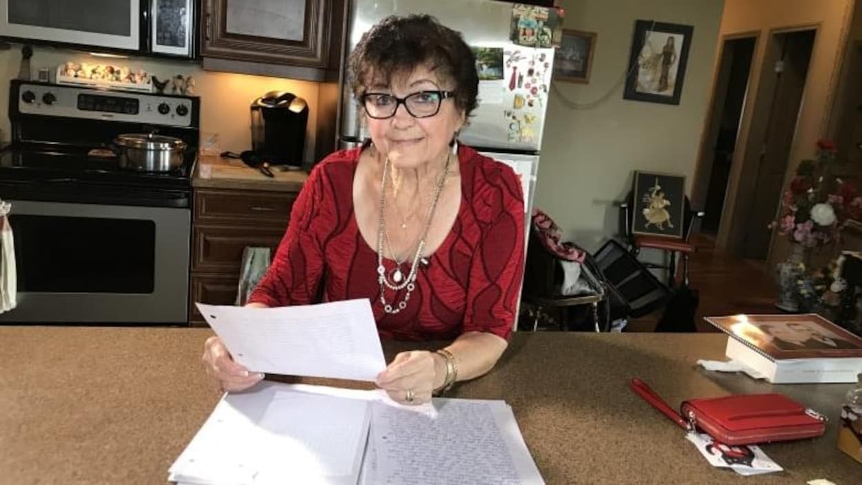 Une femme aînée s'appuie sur un comptoir en tenant la feuille d'un journal.