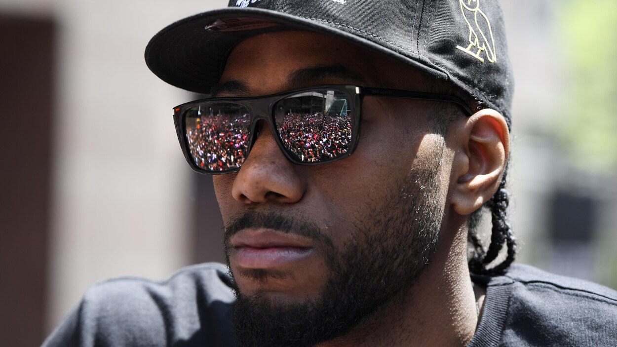 La réflexion de la foule dans les lunettes fumées d'un homme qui porte une casquette.