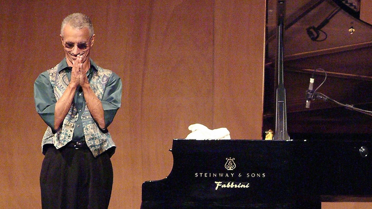 Le pianiste de jazz américain se tient debout sur scène, les mains jointes, près d'un piano de concert