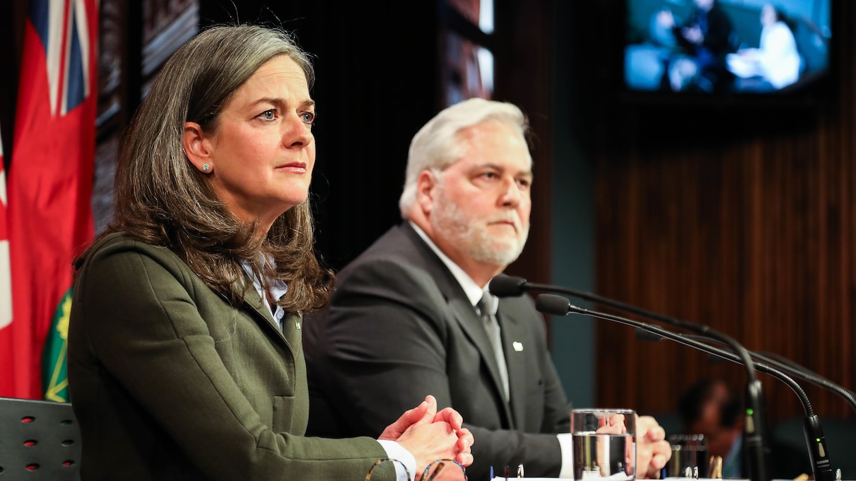 Une femme et un homme en arrière-plan à ses côtés dans une salle de presse de l'assemblée législative de l'Ontario.