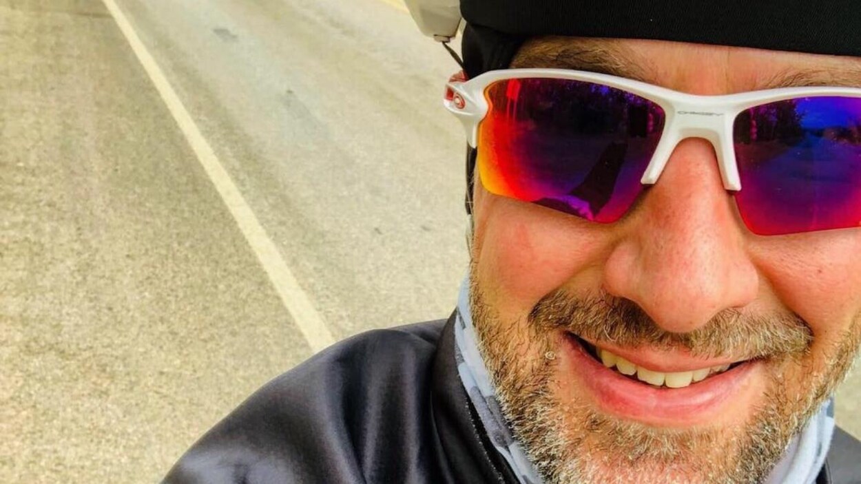 Kelly Chimilar fait un égoportrait sur son vélo. Il porte des lunettes de solei et une petite barbe.