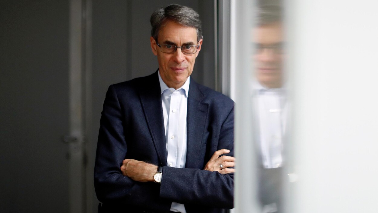 L'homme est appuyé sur une fenêtre les bras croisés et regarde l'appareil photo.