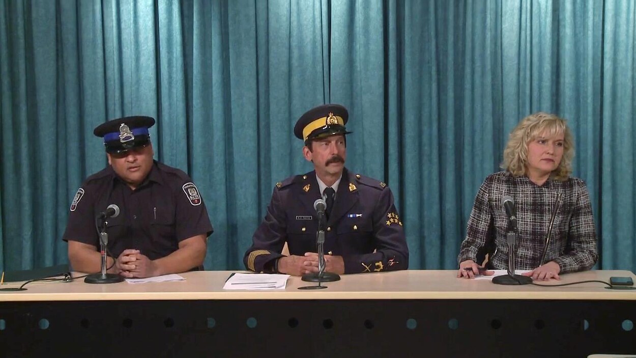 Deux policiers en uniforme et la ministre adjointe assis à une table en conférence de presse.