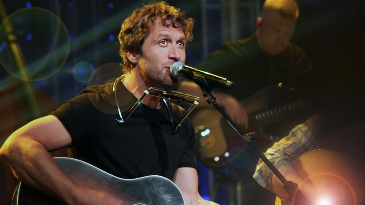 Le chanteur Kevin Parent devant un micro, guitare à la main.