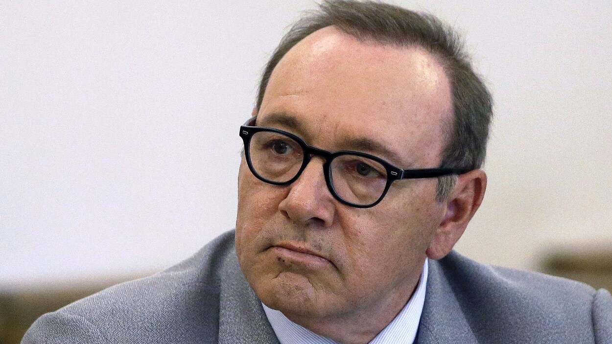 Portrait de Kevin Spacey, qui porte des lunettes et un costume gris.