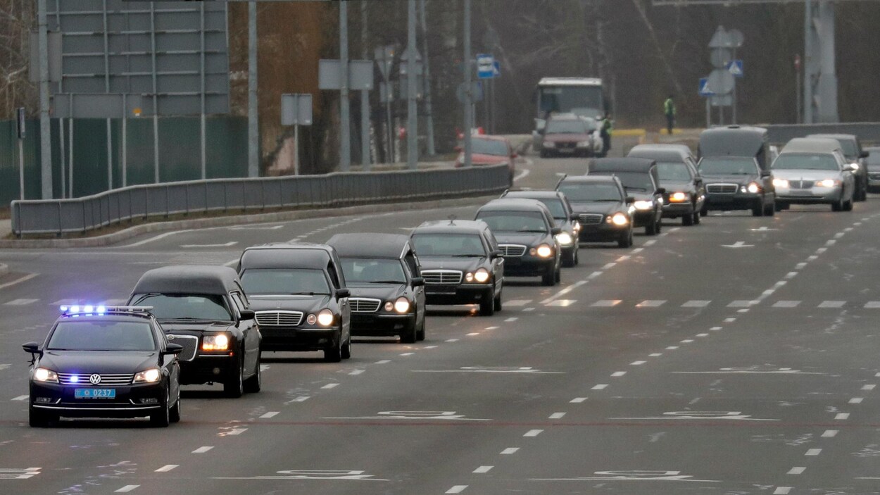 11 corbillards se suivent en file indienne sur une autoroute, précédés par une voiture de police.