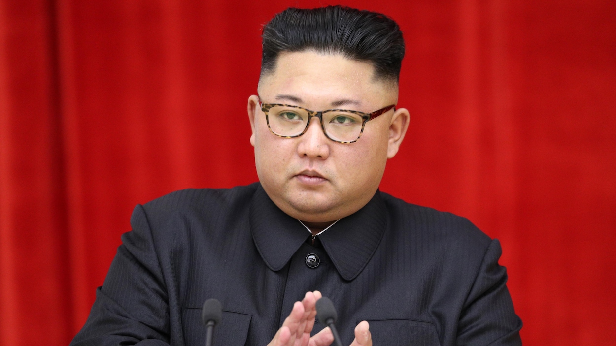 Un homme au regard sérieux et qui porte des lunettes s'apprête à faire un discours.
