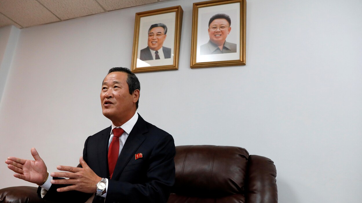 Kim Song est assis sur un fauteuil, derrière lui sont accrochés deux portraits; l'un de Kim Il-sung et l'autre de Kim Jong-il.