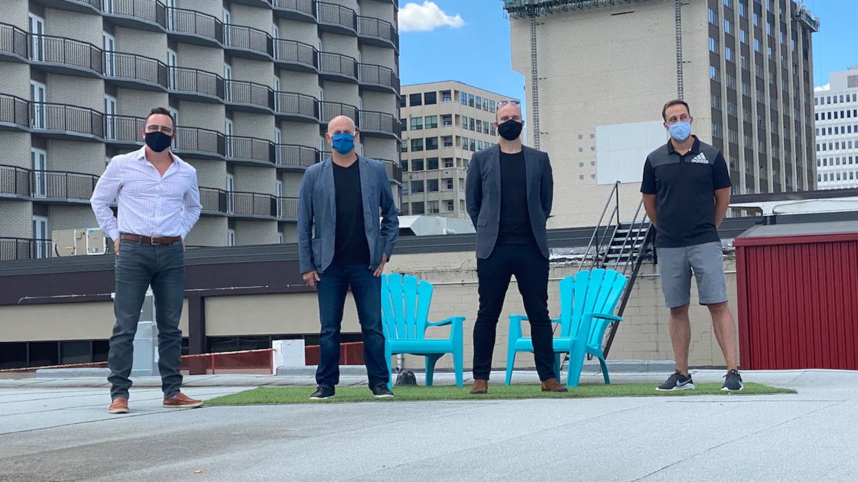 Quatre hommes alignés les uns à côté des autres sur un toit au centre-ville de Regina. Ils portent tous un masque.