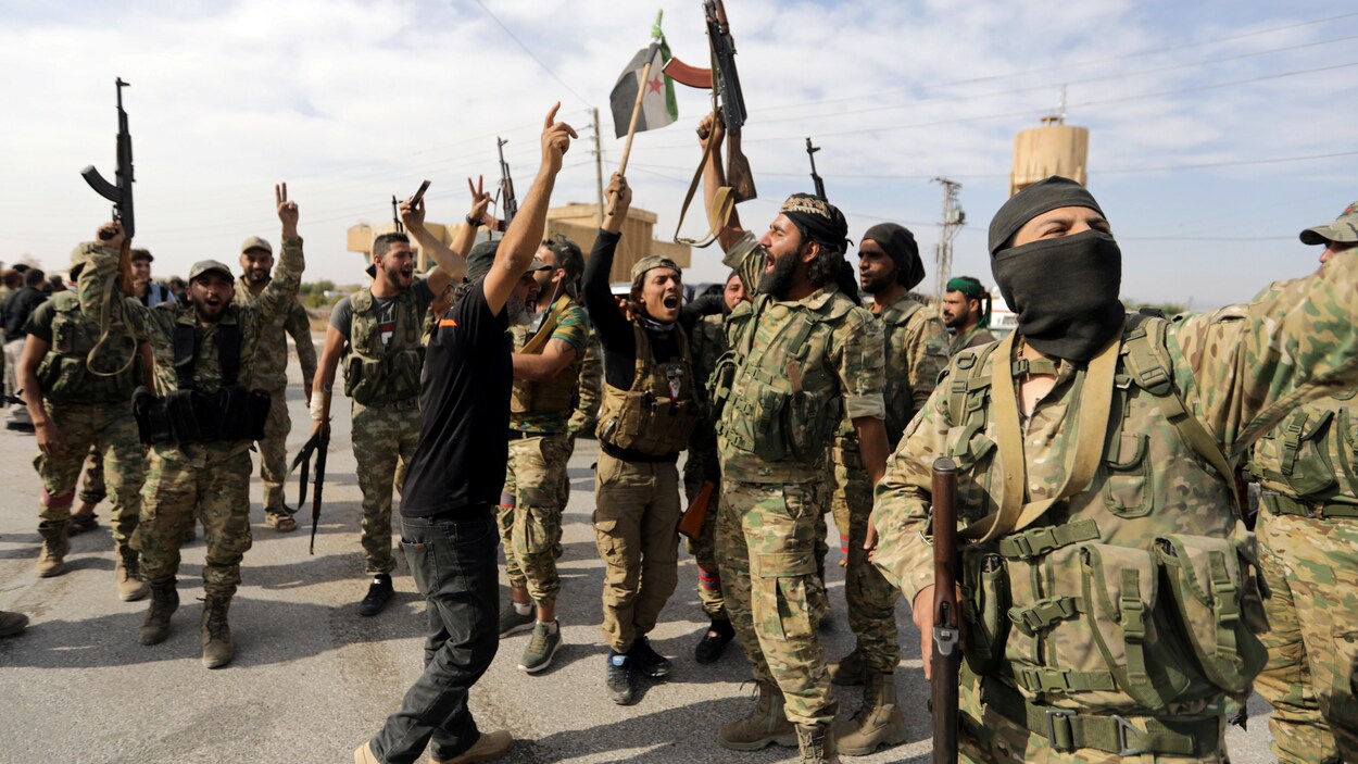 Des militaires en treillis qui brandissent leurs armes et des drapeaux syriens.