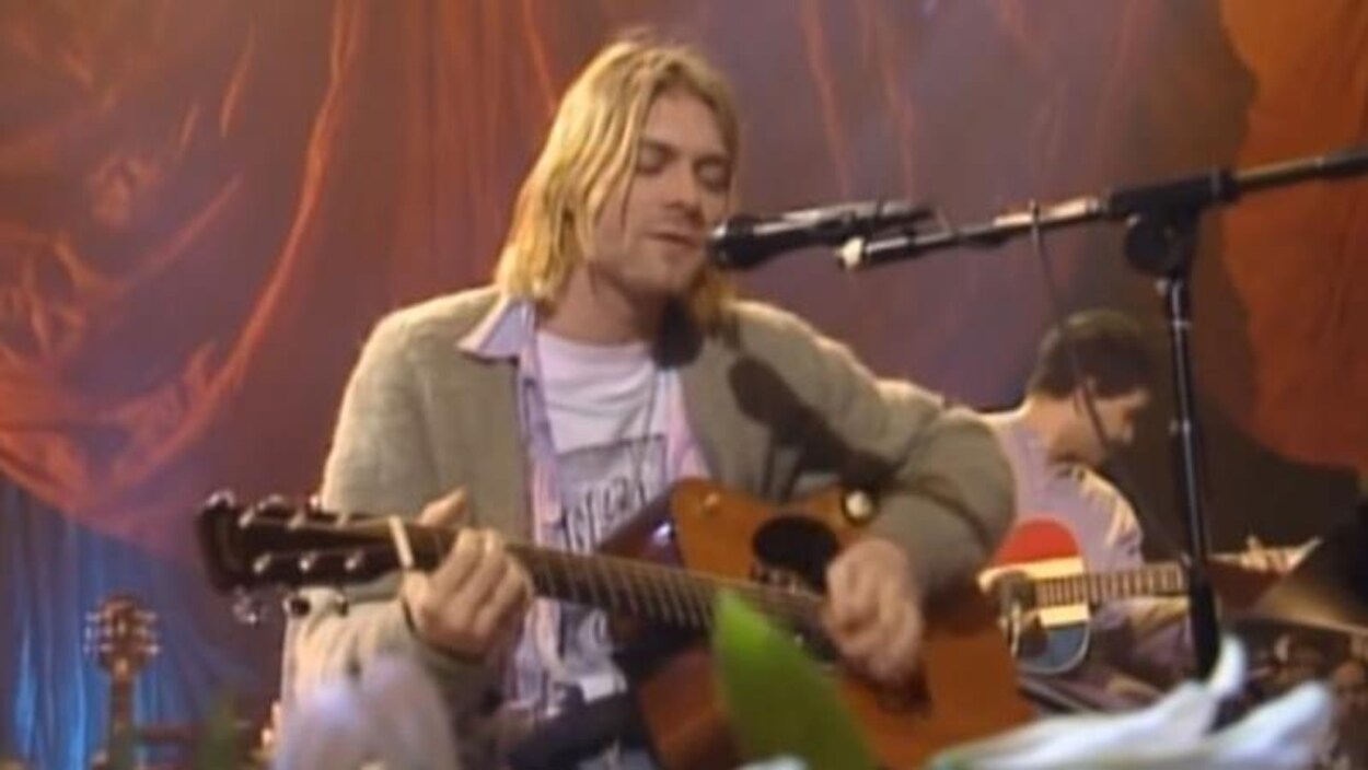 Kurt Cobain assis, chante et joue de la guitare.