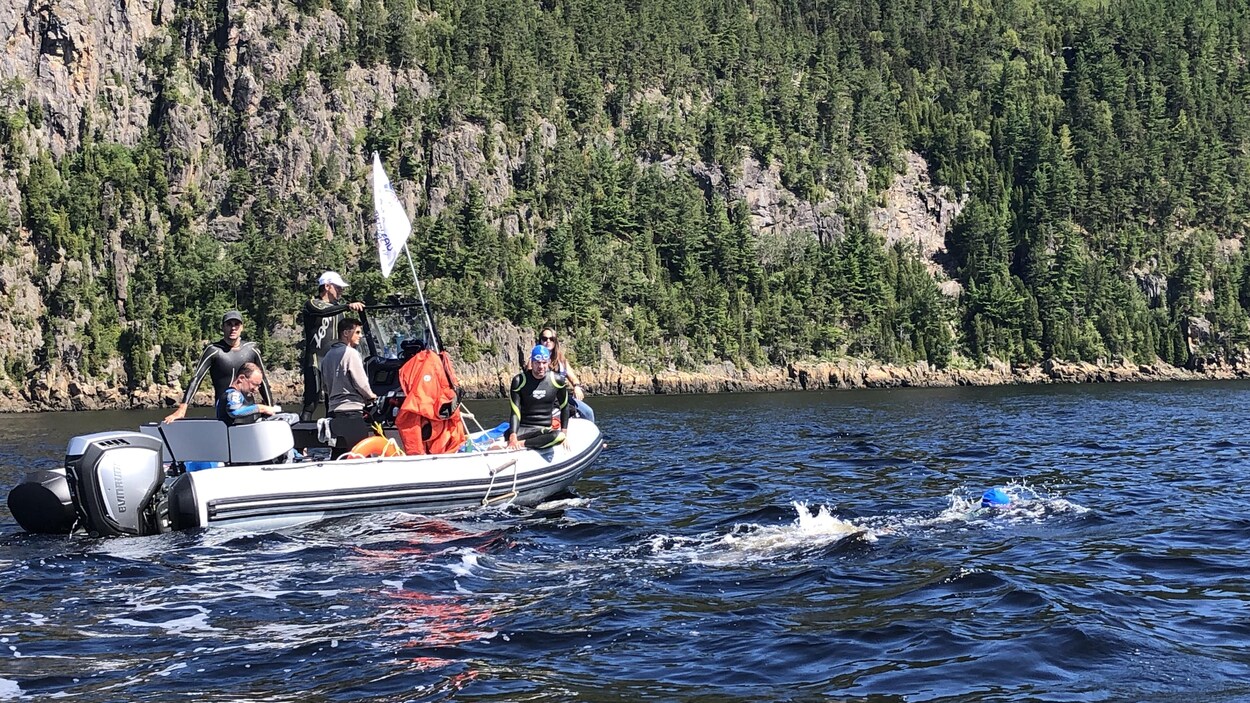 Un nageur se déplace sous les regards de ses coéquipiers qui se trouvent à bord d'un petit bateau.