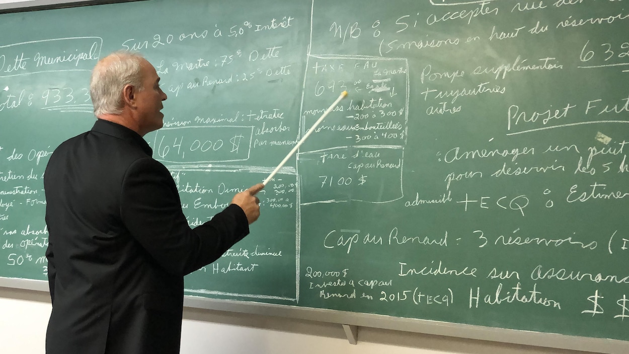Un homme devant un tableau noir rempli d'explications écrites à la craie