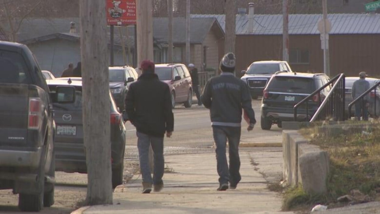 Deux personnes, vues de dos, en train de marcher sur un trottoir dans la ville de La Ronge.
