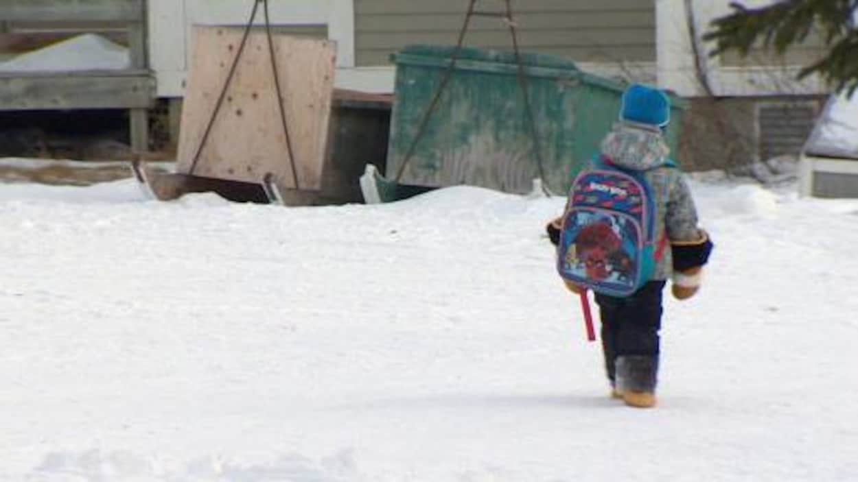 Un enfant marche dans la neige avec son sac d'école.