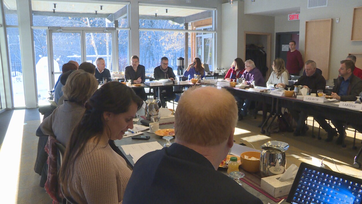 Des personnes assises autour d'une table dans une salle éclairée par la lumière du jour.