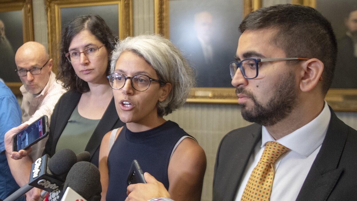 Les trois intervenants sont entourés de journalistes.
