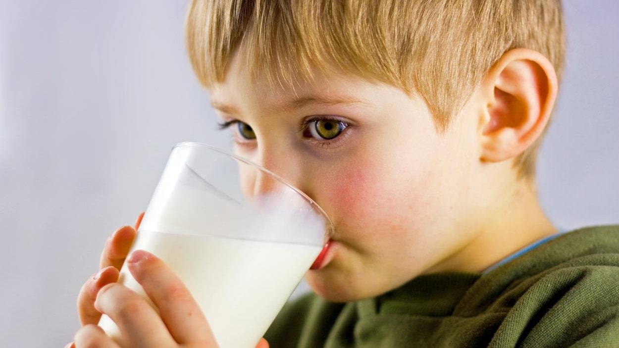 Un petit garçon boit un verre de lait.