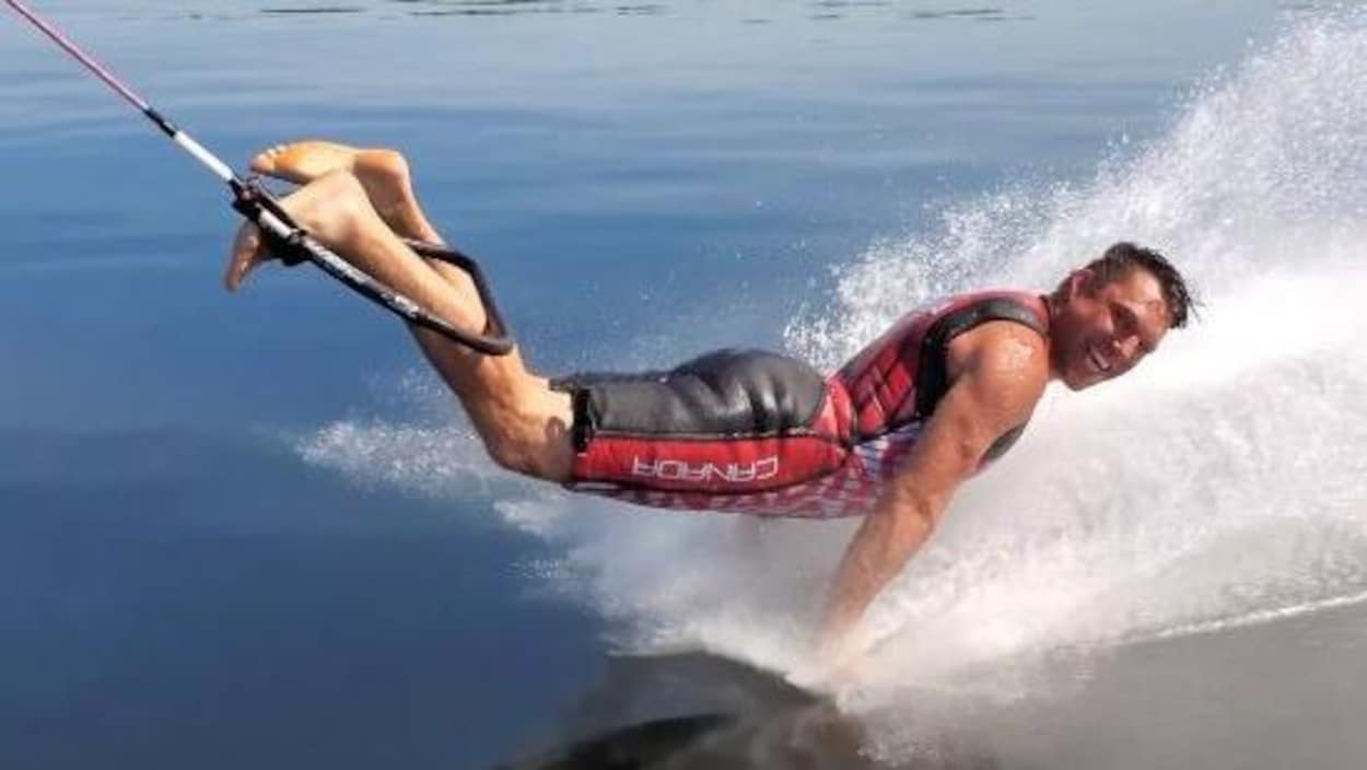 Un homme accroché à une corde de ski nautique par les pieds fait des pompes directement sur l'eau.