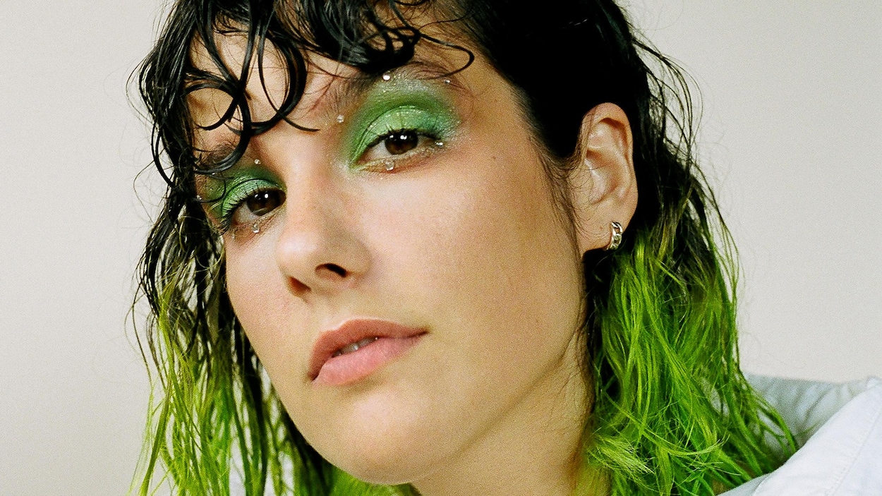 Une jeune femme avec des cheveux colorés vert fluo regarde l'objectif.
