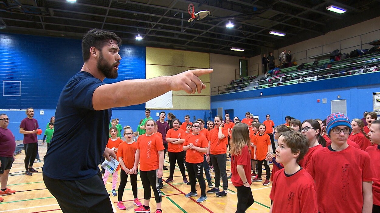 Laurent Duvernay-Tardif parle à un groupe d'élèves assemblés devant lui, dans un gymnase.