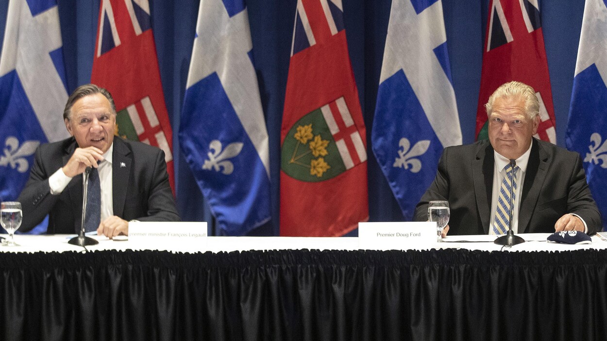 François Legault et Doug Ford assis à une table devant des drapeaux.