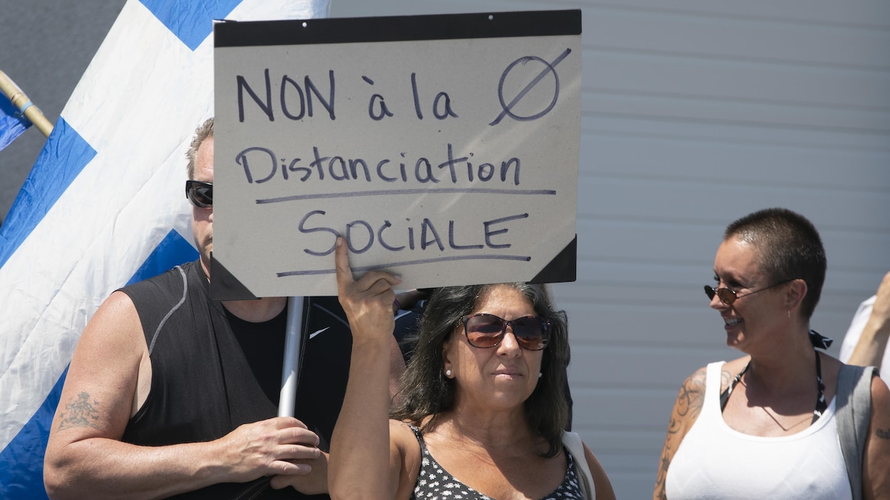 Des manifestants, dont une femme qui tient une pancarte sur laquelle est écrit : Non à la distanciation sociale.