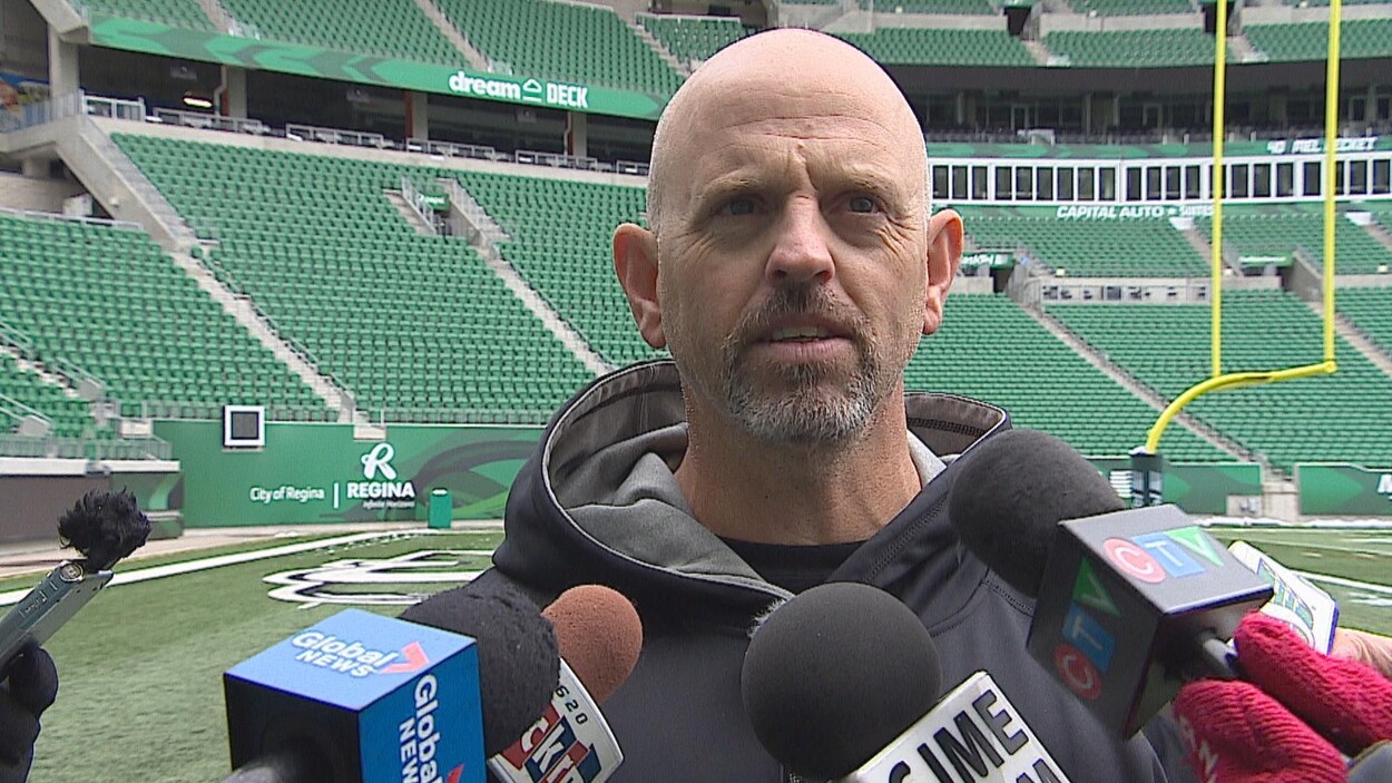 Plan moyen de Craig Dickenson donnant une entrevue debout sur la pelouse du stade Mosaic à Regina.