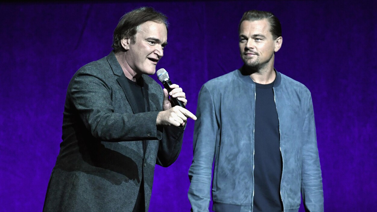 Quentin Tarantino s'adresse au public du CinemaCon pendant que Leonardo DiCaprio le regarde. Quentin Tarantino s'adresse au public du CinemaCon pendant que Leonardo DiCaprio le regarde.
