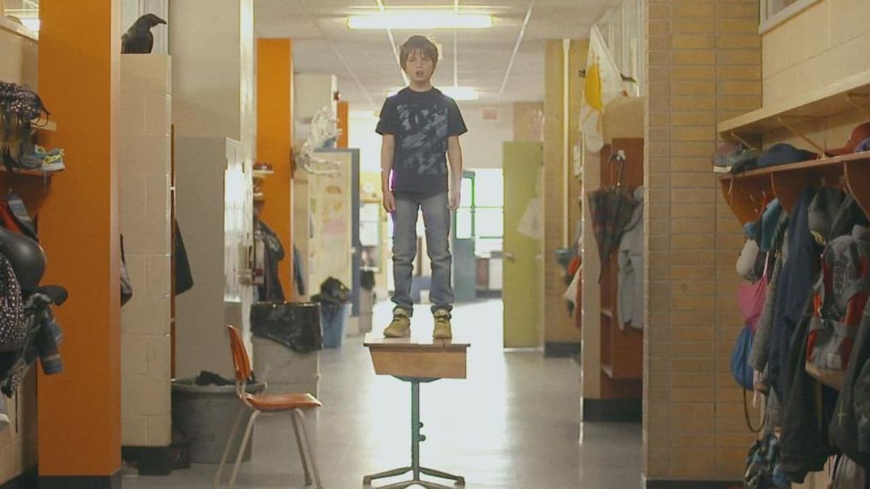Un garçon est debout sur un pupitre dans le couloir d'une école.