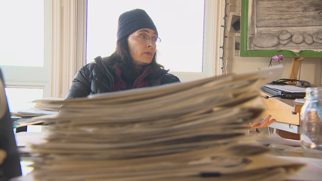 Liane Tessier assise devant une pile de documents sur un bureau. Liane Tessier assise devant une pile de documents sur un bureau.
