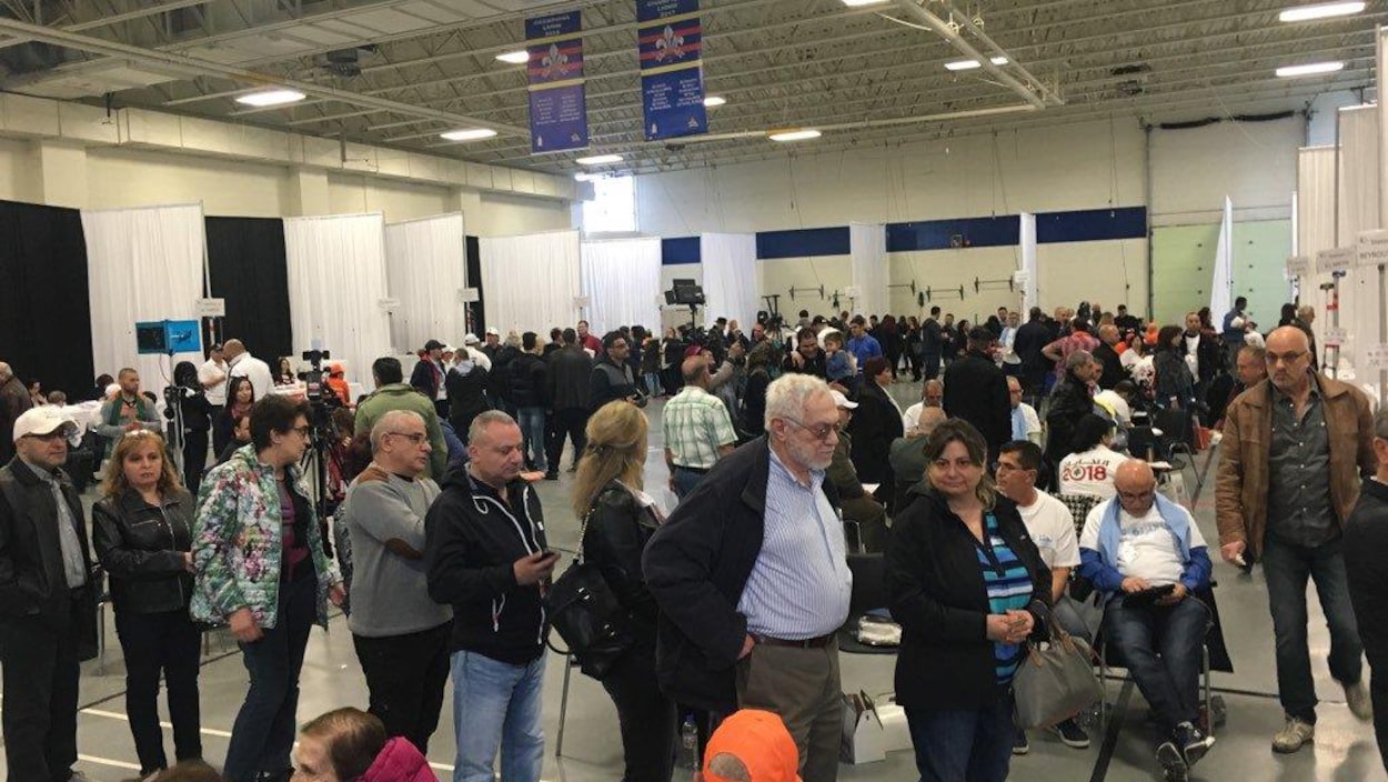 Des hommes et des femmes de tous les âges faisant la file à l'intérieur du bureau de vote à Laval.