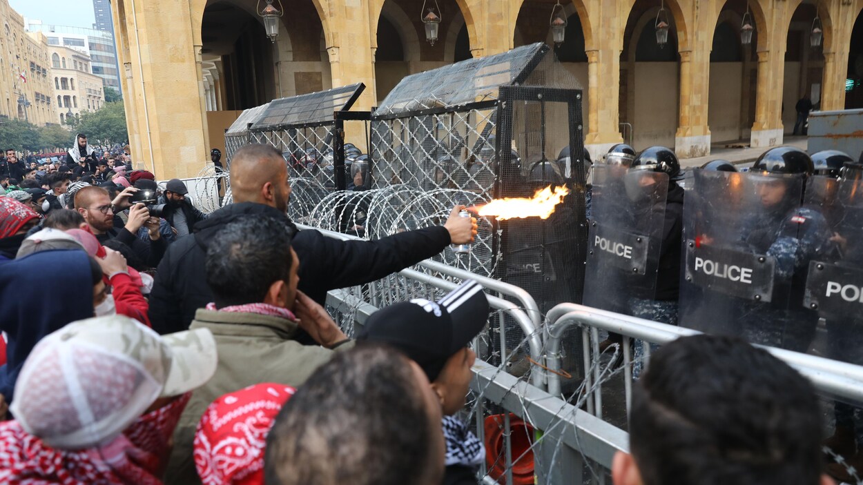 Des manifestants sont derrière des clôtures de métal et des policiers en tenue antiémeute.