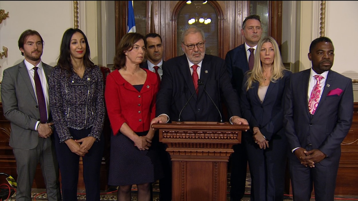 Pierre Arcand au lutrin, entouré de sept députés libéraux. Pierre Arcand au lutrin, entouré de sept députés libéraux.