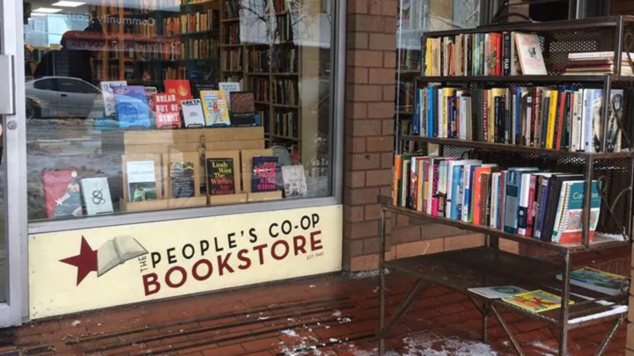 Des livres empilés sur trois étagères devant la vitrine de la librairie The People's Co-op