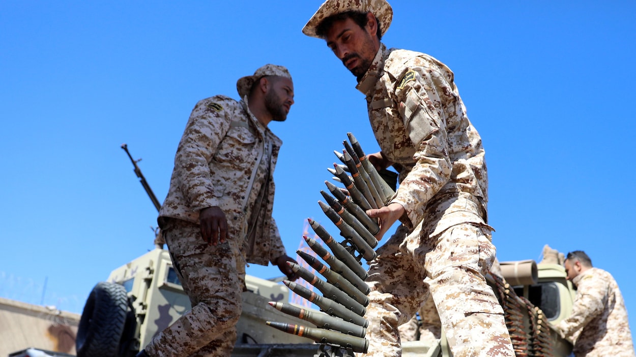 Un homme en treillis militaire prend des munitions près de véhicules blindés.