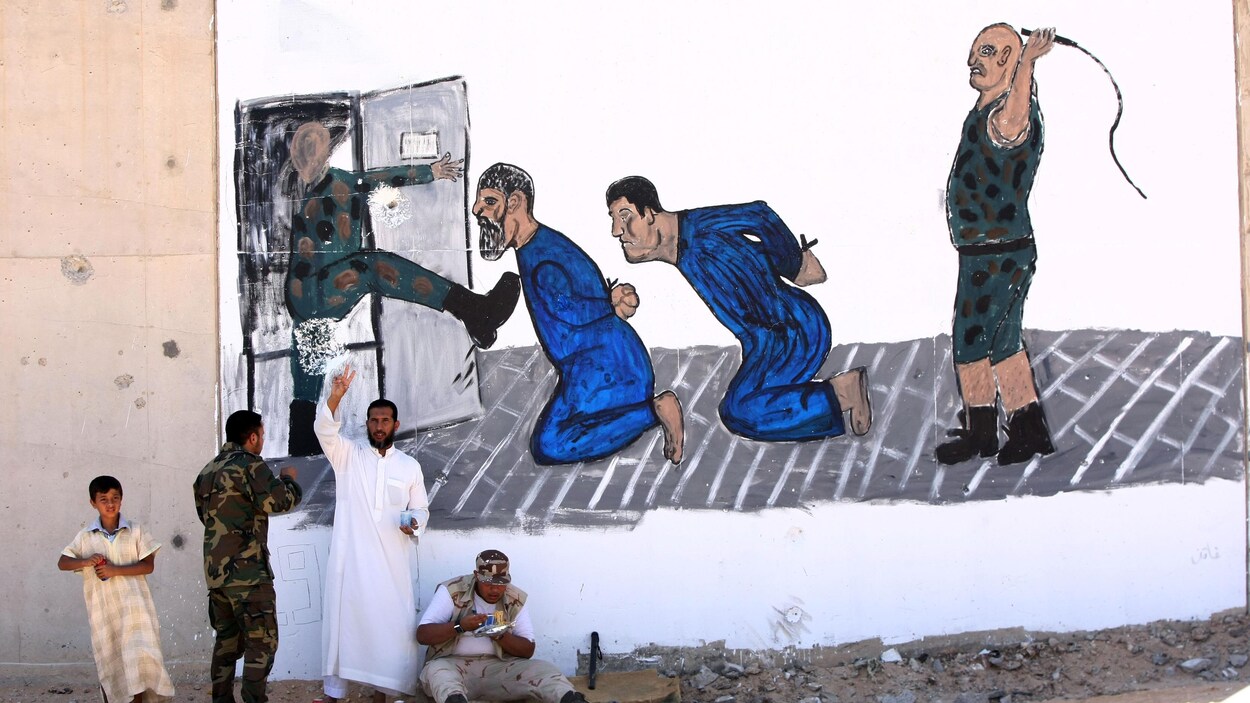 Des Libyens, devant une murale commémorant un massacre de prisonniers survenu à la prison d'Abou Slim. Des Libyens, devant une murale commémorant un massacre de prisonniers survenu à la prison d'Abou Slim.