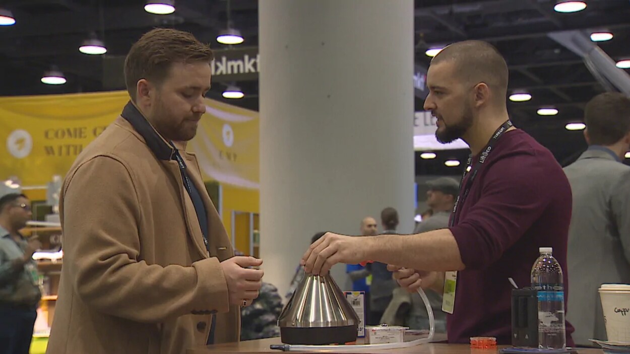 Un exposant du salon Lift & Co. discute avec un client devant un objet en métal qui ressemble à une théière.