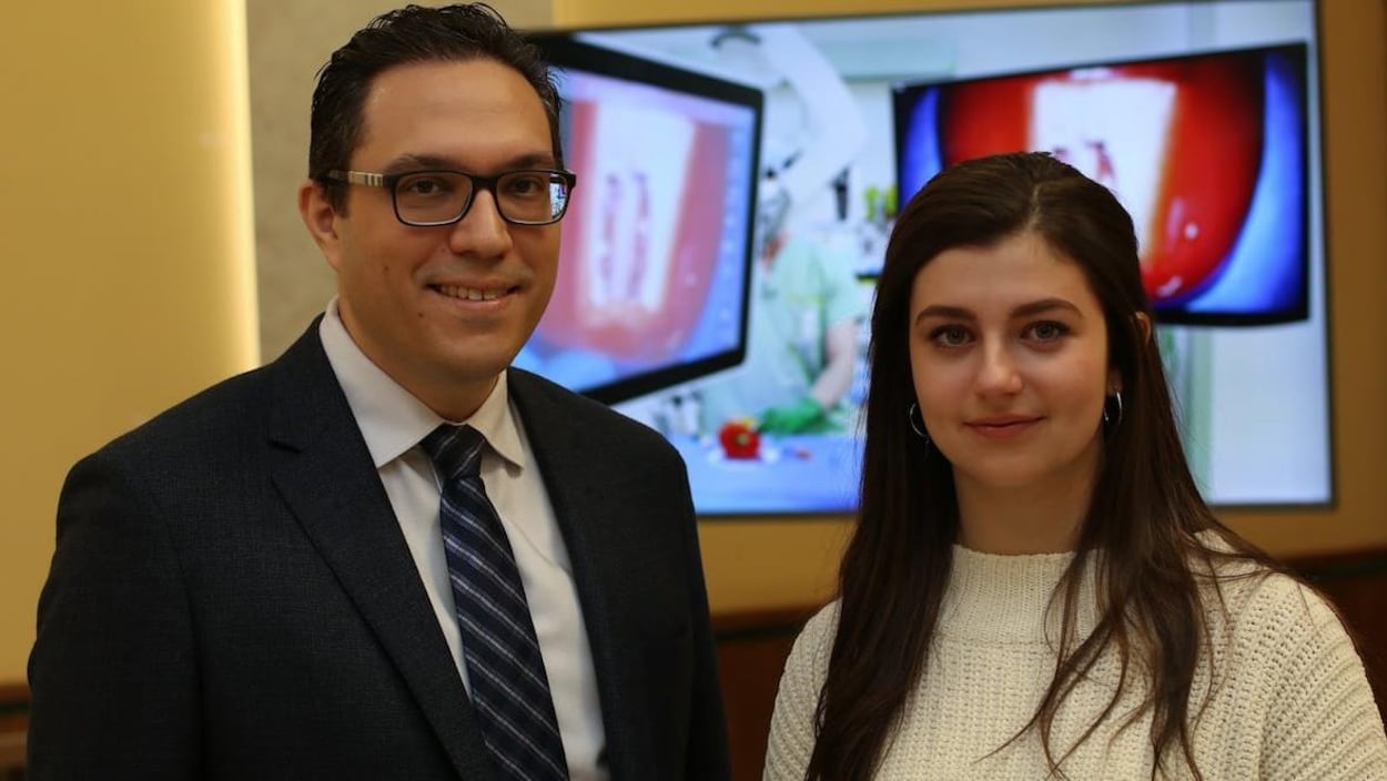 Un homme en costume portant des lunettes et une jeune femme avec un chandail blanc.