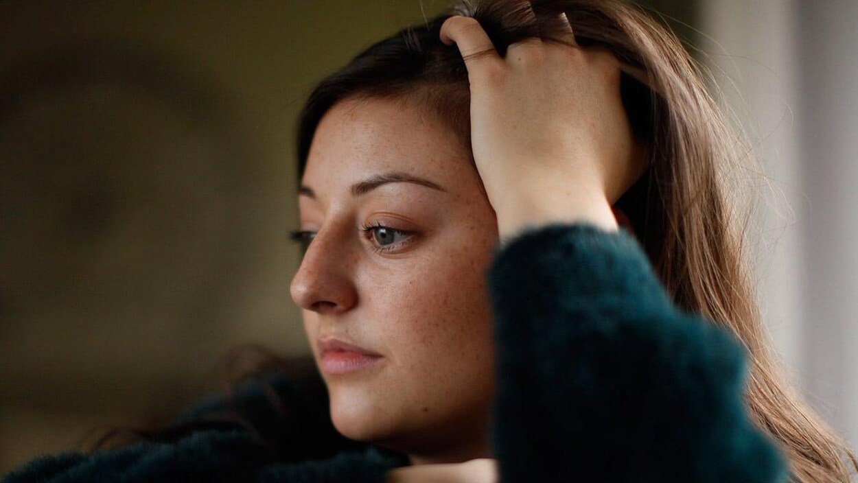 La jeune femme est assise, la tête appuyée contre sa main. Elle regarde droit devant elle, comme plongée dans ses pensées.