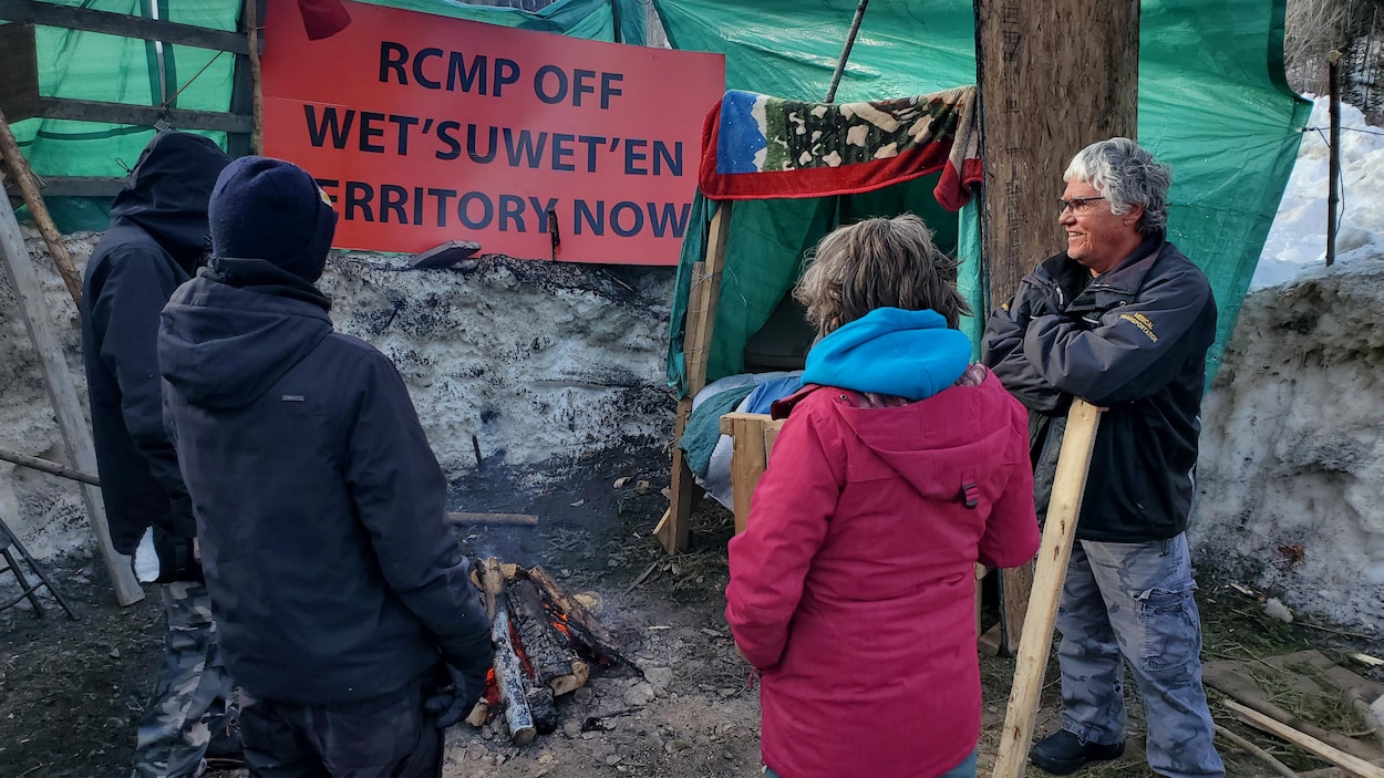 Quatre personnes discutent autour d'un feu sur le site du campement érigé sur la voie ferrée.
