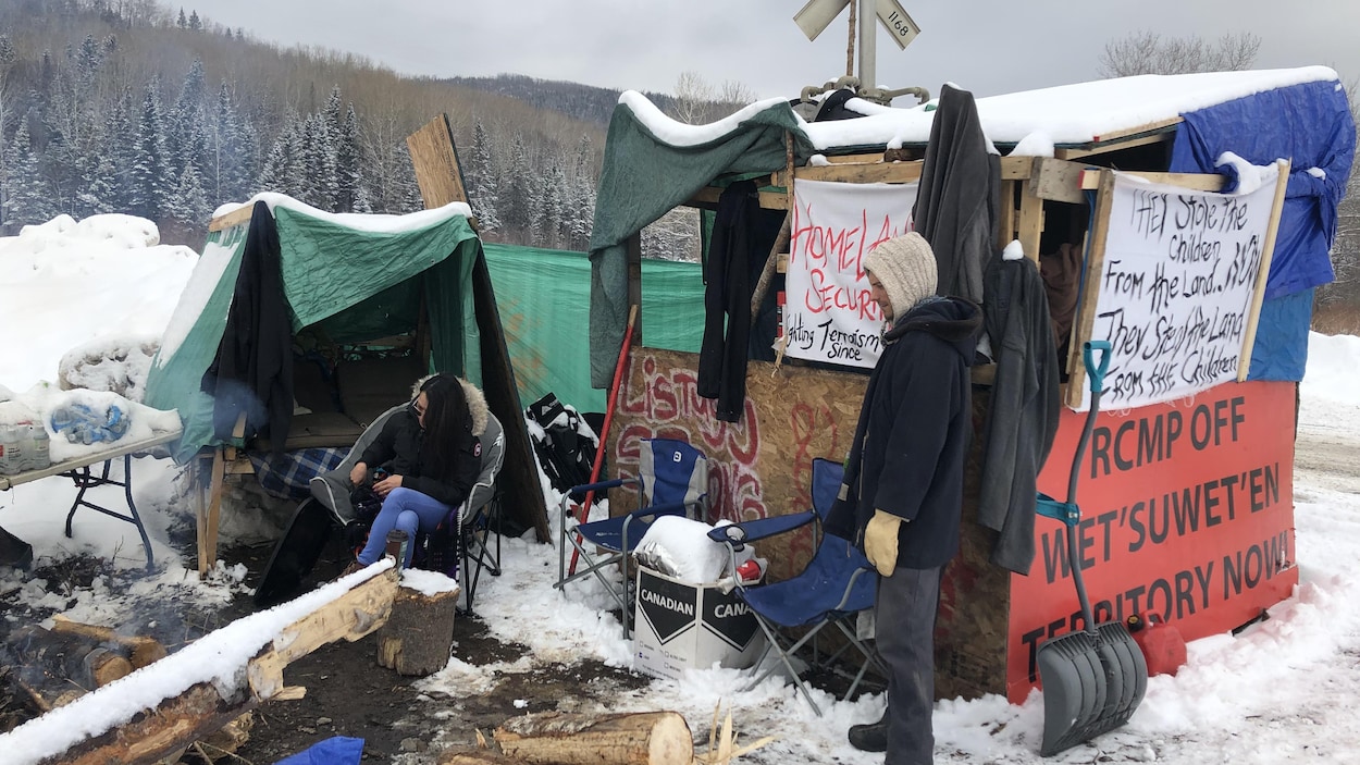 Une femme est assise et un homme se tient debout au campement érigé près de la voie ferrée à Listuguj, le 3 mars 2020.