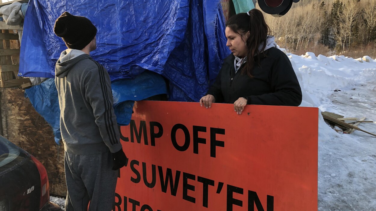 Des gens qui enlèvent une affiche installée sur le campement des Micmacs de Listuguj.