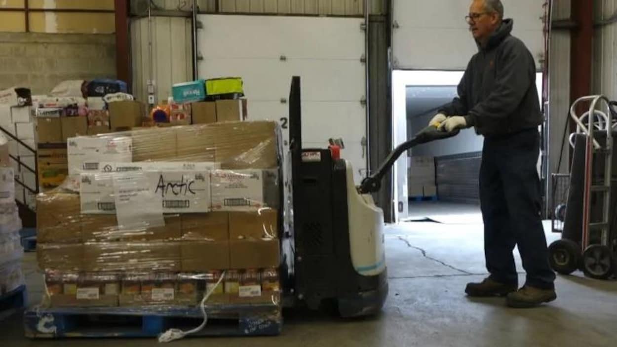 Un homme dans un hangar pousse des boîtes entassées sur lesquelles ont peut lire « Arctic »