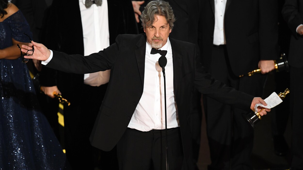 L'homme écarte les bras en tenant la statuette.
