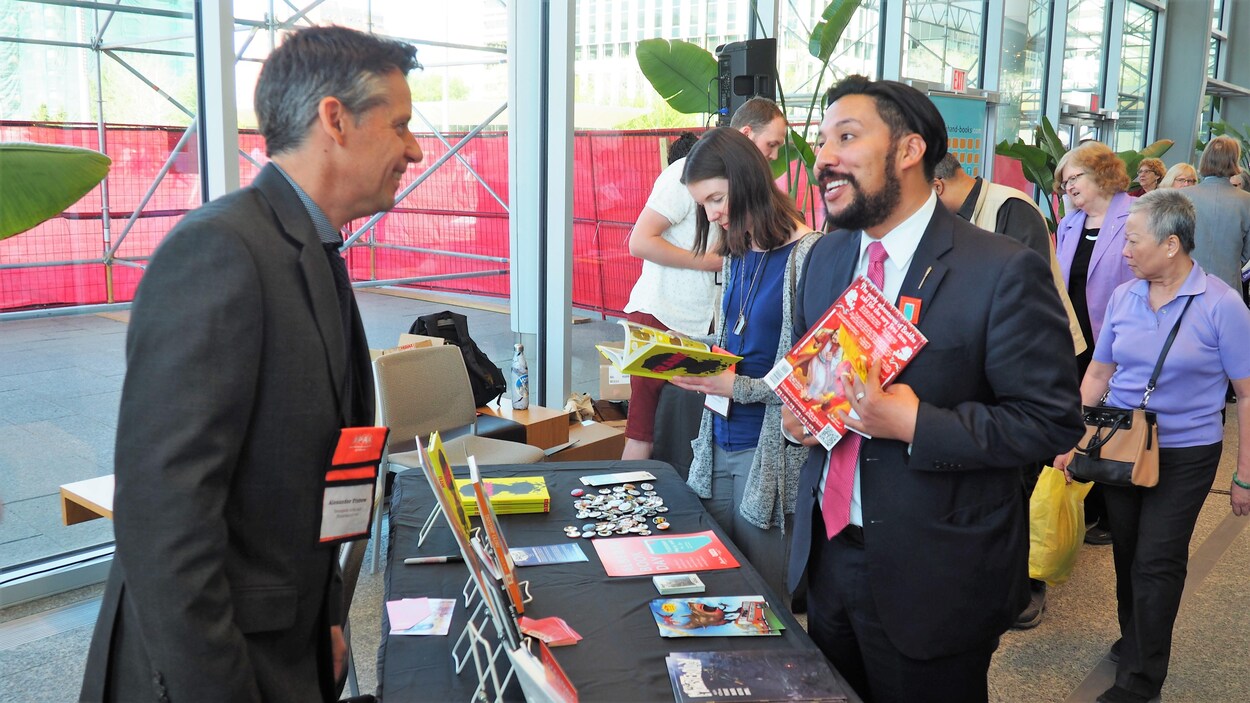 Un éditeur discute avec le ministre de la Culture et du Tourisme, Ricardo Miranda. Le ministre tient un magazine dans la main. Derrière lui, une foule regarde les stands de livres. Un éditeur discute avec le ministre de la Culture et du Tourisme, Ricardo Miranda. Le ministre tient un magazine dans la main. Derrière lui, une foule regarde les stands de livres.